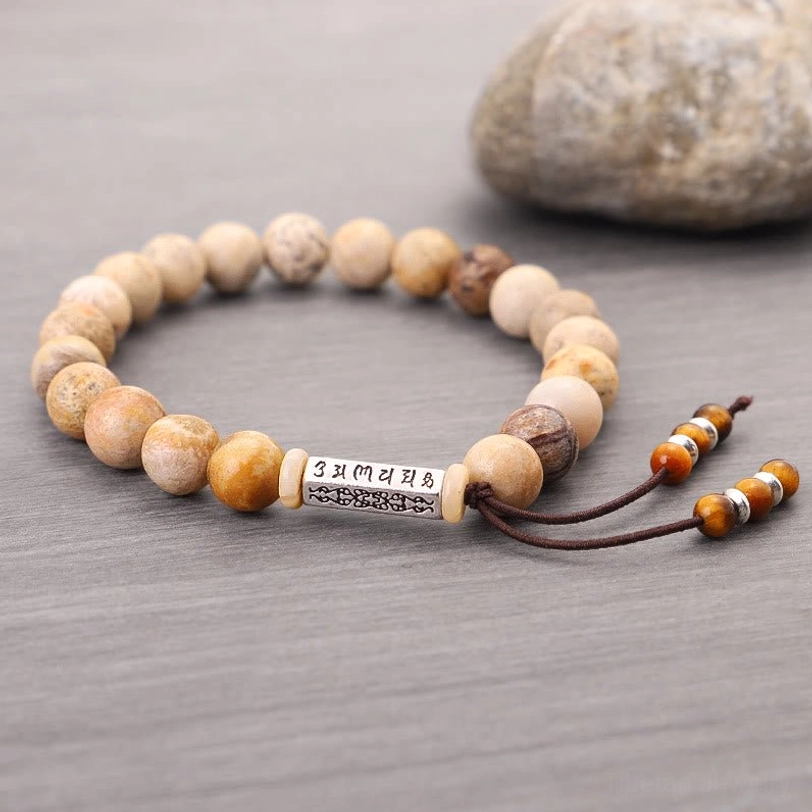 Natural weathered stone mantra bracelet on natural background, showing earthy bead tones and silver charm accent