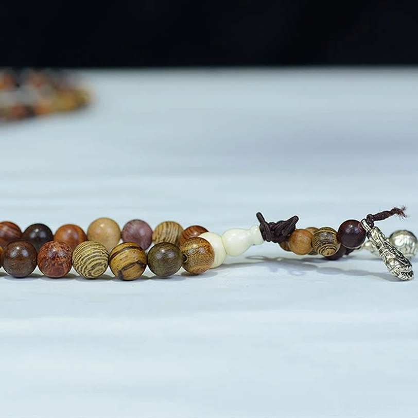 Partial natural wood mala strand flat lay on light blue background showing wood grain patterns and silver pendant
