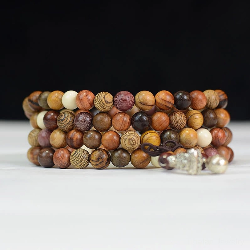 Stacked natural wood mala bracelets flat lay showing assorted wood bead tones with white accents and silver tassel