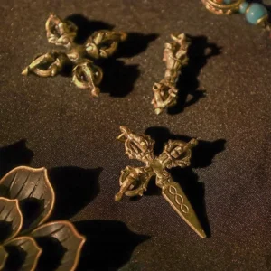 Multiple Tibetan brass double dorje and single dorje vajra pendants - traditional Buddhist ritual objects with aged bronze finish displayed on dark fabric