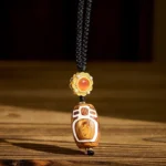Nine-eye dzi bead agate pendant necklace with gold clasp on wooden table showing carved white sacred pattern