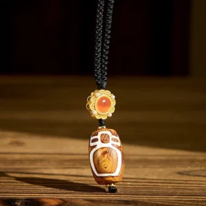 Nine-eye dzi bead agate pendant necklace with gold clasp on wooden table showing carved white sacred pattern