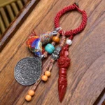Tibetan Nine-Eye Dzi Bead Bagua keychain with red braided rope, silver plaque, and carved red ritual pendant on wooden surface