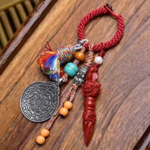 Tibetan Nine-Eye Dzi Bead Bagua keychain with red braided rope, silver plaque, and carved red ritual pendant on wooden surface