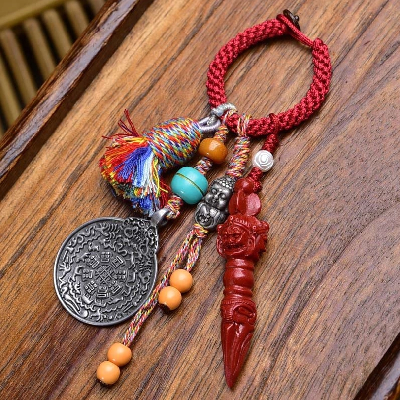 Tibetan Nine-Eye Dzi Bead Bagua keychain with red braided rope, silver plaque, and carved red ritual pendant on wooden surface