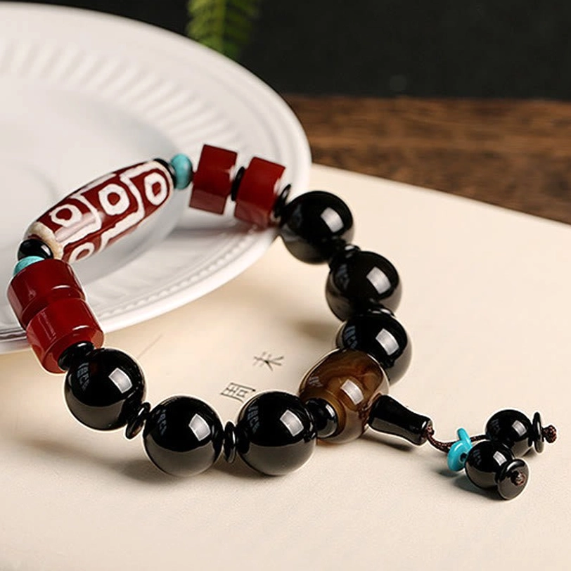 Handcrafted Nine-Eye Dzi Bead bracelet with Black Onyx stones and turquoise bead details on light wooden surface - traditional Tibetan spiritual protection jewelry