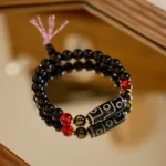 Nine-eye dzi bead black onyx bracelet with gold spacers and pink tassel on wooden surface