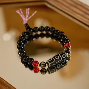 Nine-eye dzi bead black onyx bracelet with gold spacers and pink tassel on wooden surface
