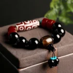 Nine-Eye Dzi Bead Black Onyx Bracelet with turquoise accent displayed on dark wooden surface with green foliage - close-up overhead view showing intricate bead patterns and protective amulet details