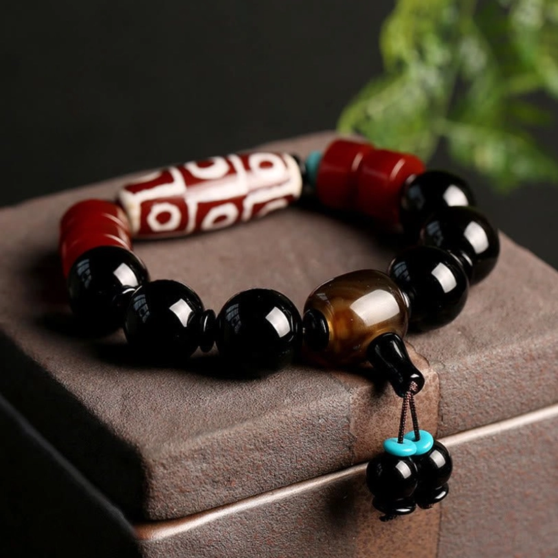 Nine-Eye Dzi Bead Black Onyx Bracelet with turquoise accent displayed on dark wooden surface with green foliage - close-up overhead view showing intricate bead patterns and protective amulet details
