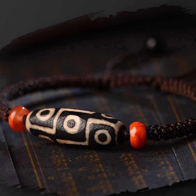 Nine-Eye Dzi bracelet overhead close-up on Tibetan cloth background, displaying intricate nine-eye bead pattern and spiritual design
