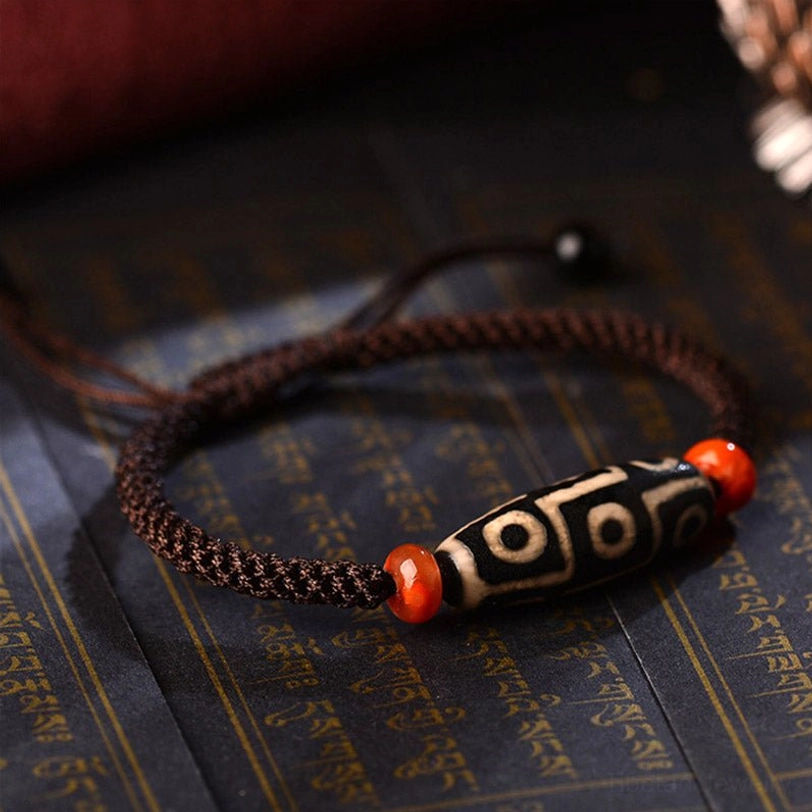 Nine-Eye Dzi bracelet overhead close-up on Tibetan scripture background, highlighting sacred bead pattern and handcrafted details