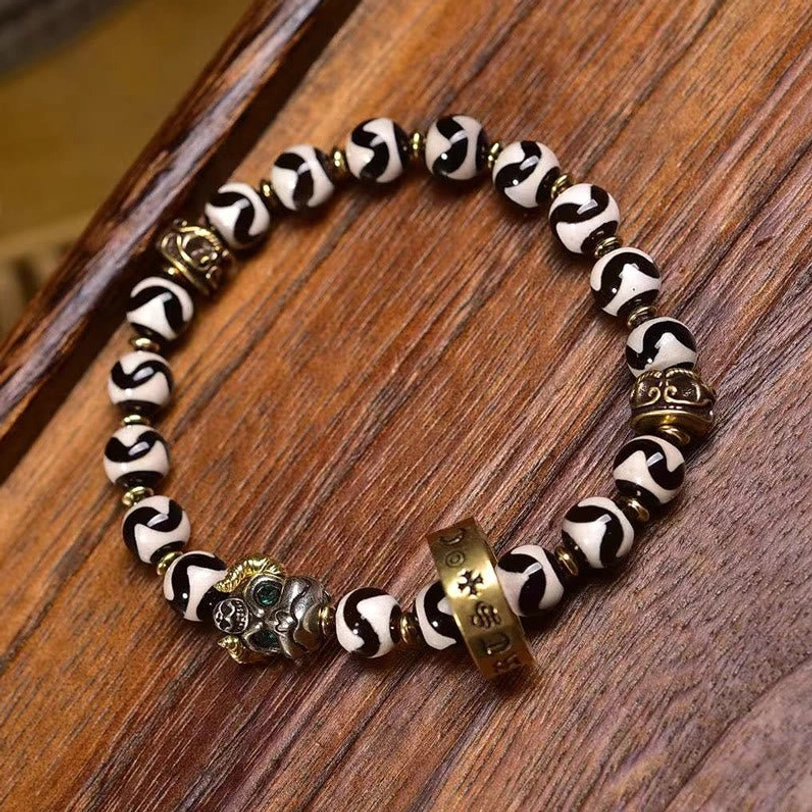 Tibetan dzi bead bracelet flat lay featuring black and white striped sacred beads with vintage brass decorative elements