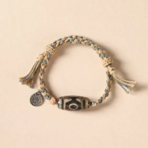 Nine-eye Dzi bead Tibetan protection bracelet with beige-blue braided rope, metal charm, and hand-painted sacred stone bead on light background