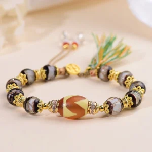 Nine-Eye Dzi bead blessing bracelet flat lay with gold hardware and green tassel on light background