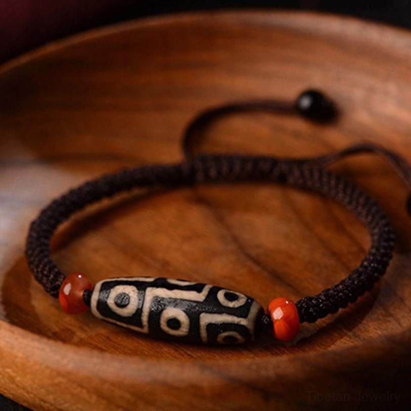 Nine-Eye Dzi bracelet side view on plain wooden plate, showing premium braided cord and authentic bead craftsmanship