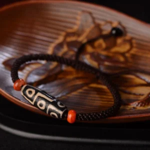 Nine-Eye Dzi bead bracelet side view on carved wooden surface, displaying intricate bead details and adjustable braided string design