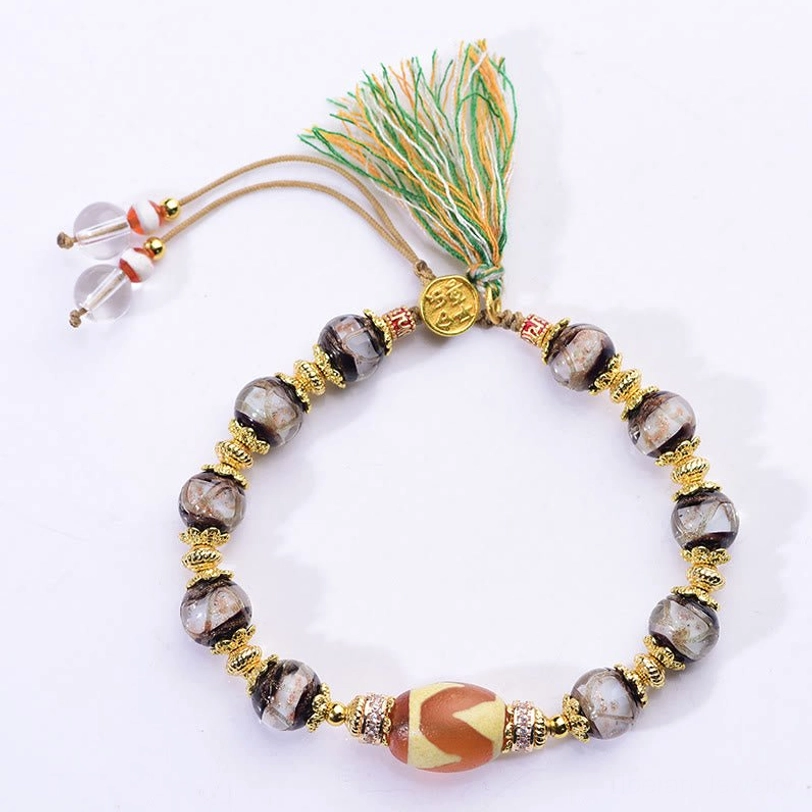 Dzi bead bracelet with sliding adjustable knot and decorative tassel on plain light background