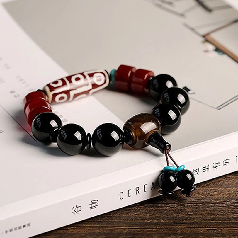 Handmade Nine-Eye Dzi Bead Black Onyx Bracelet on vintage book with natural wooden background - demonstrating spiritual amulet design and beadwork craftsmanship