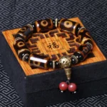 Nine-eye dzi bead bracelet displayed on traditional wooden gift box with fu character, showing brown-black agate beads with gold metal spacers and red bead tassel - top view