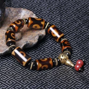 Tibetan nine-eye dzi bead bracelet close-up on stone slab and patterned fabric, highlighting cylindrical eye-patterned beads and metal spacer details - side angle