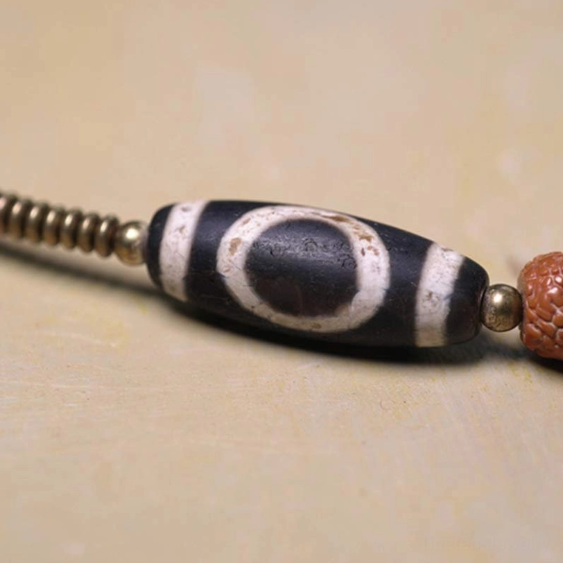 Close-up of hand-painted Nine-Eye Dzi Bead showing traditional black and white eye pattern with metal spacer beads