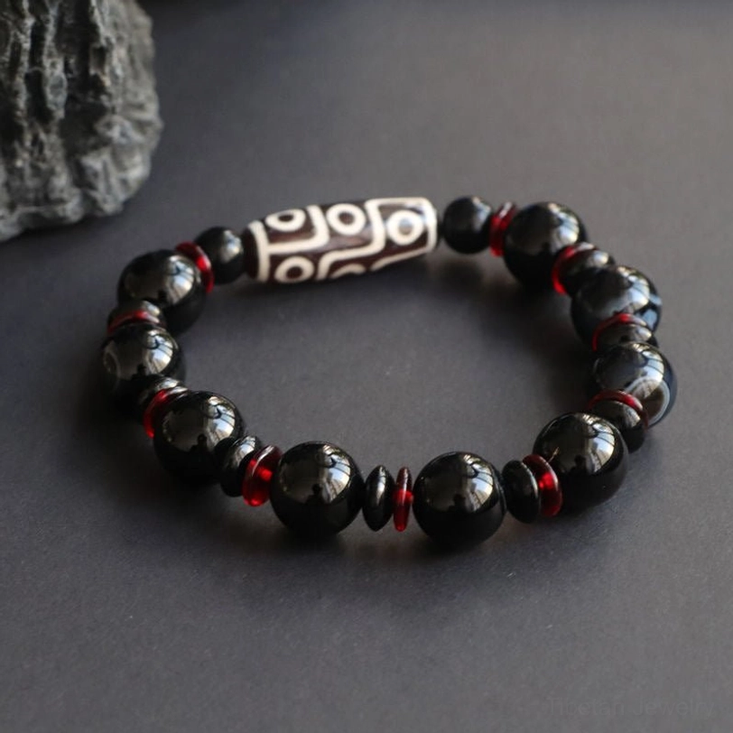 Complete view of Black Onyx Nine-Eye Dzi Bead protection bracelet arranged on natural stone surface, showing the symmetrical bead layout and centered Dzi focal point