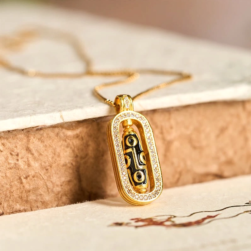 24K gold plated nine-eye dzi bead pendant with zircon frame on vintage paper background, flat lay close-up view