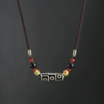 Nine-eye dzi bead necklace with brown braided rope and gold black red decorative beads on dark background