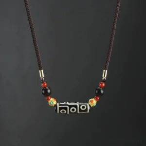 Nine-eye dzi bead necklace with brown braided rope and gold black red decorative beads on dark background