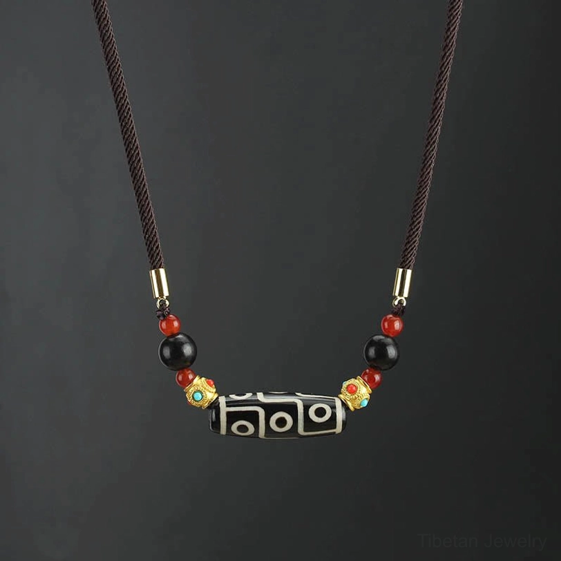 Nine-eye dzi bead necklace with brown braided rope and gold black red decorative beads on dark background