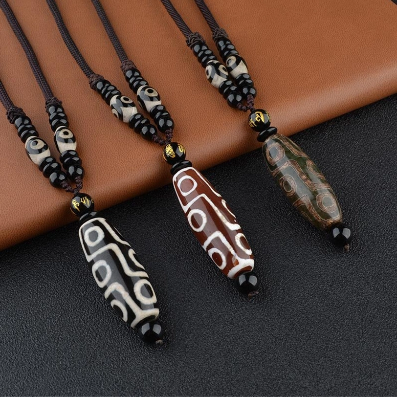 Multiple handcrafted nine-eye Dzi bead necklaces in different colors displayed on brown leather, showcasing traditional Tibetan agate pendant designs