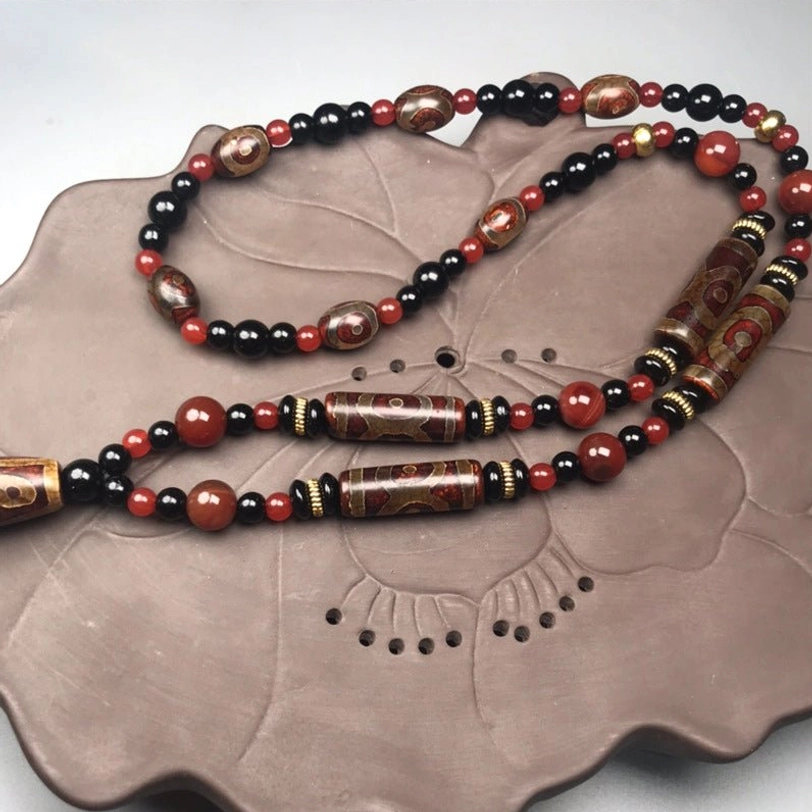 Long Nine-Eye Dzi Bead Tibetan necklace with multiple dzi beads in warm earthy tones, arranged on lotus-carved ceramic display