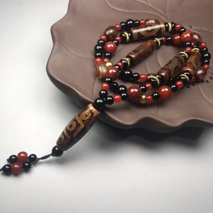 Nine-Eye Dzi Bead necklace with large polished central accent beads, leaning against dark ceramic teapot in side flat lay