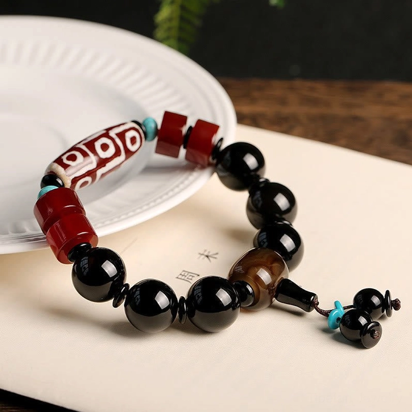 Nine-Eye Dzi Bead Black Onyx Bracelet with turquoise accent pendant on white plate and light wood surface - authentic Tibetan spiritual jewelry flat lay