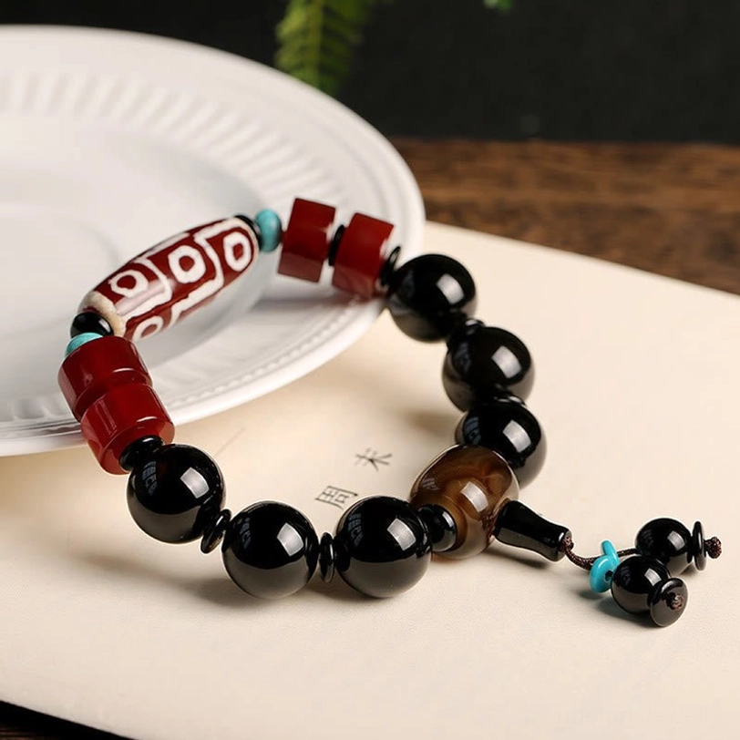 Tibetan Nine-Eye Dzi Bead bracelet with Black Onyx beads and turquoise pendant on white ceramic plate - flat lay product photography showing wrist circumference and natural bead texture