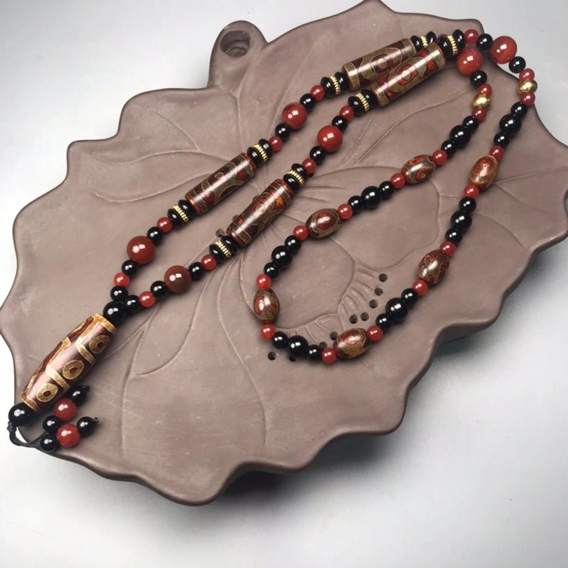 Nine-Eye Dzi Bead Red Agate Necklace with intricate Tibetan dzi patterns displayed on lotus ceramic tray, overhead flat lay view
