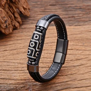 Black Nine-Eye Dzi Bead leather bracelet with gun-metal hardware and adjustable buckle, displayed on wooden surface with natural pine cone styling