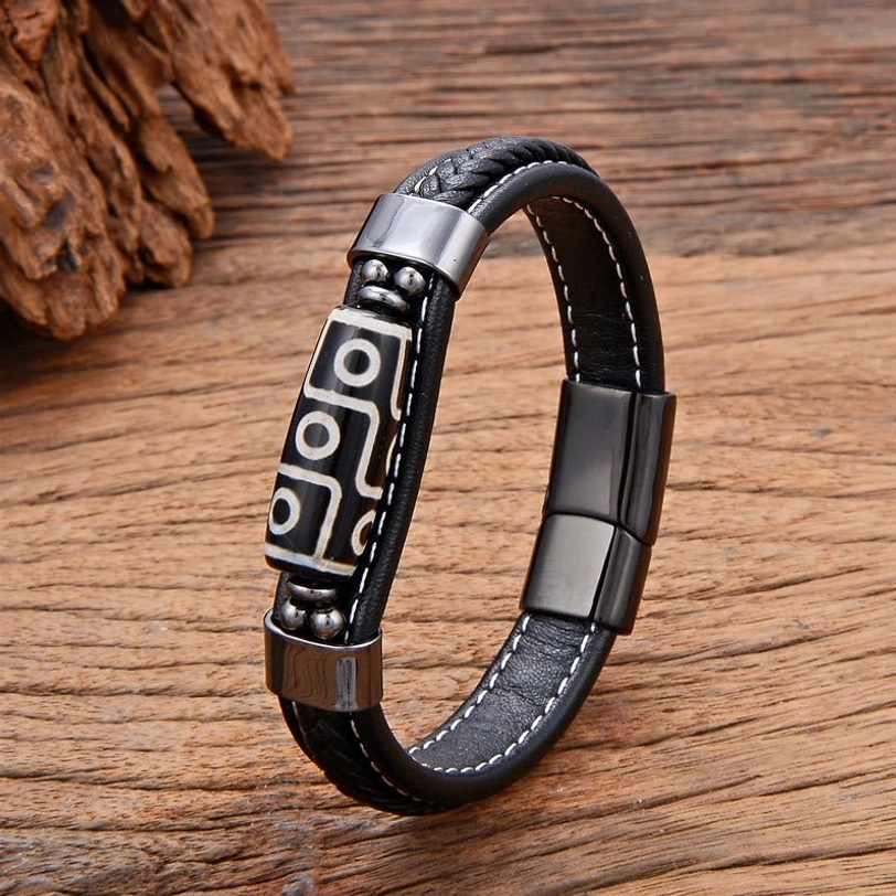 Black Nine-Eye Dzi Bead leather bracelet with gun-metal hardware and adjustable buckle, displayed on wooden surface with natural pine cone styling