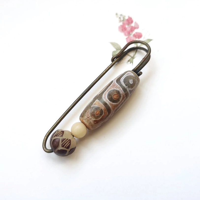 Nine-eye dzi bead bodhi seed lotus brooch flat lay on white background, showing intricate carved patterns and antique bronze safety pin