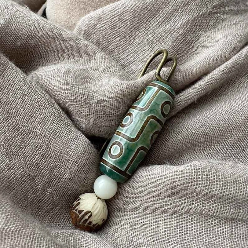 Green nine-eye dzi bead bodhi seed lotus brooch on linen fabric, showing teal green dzi bead variant