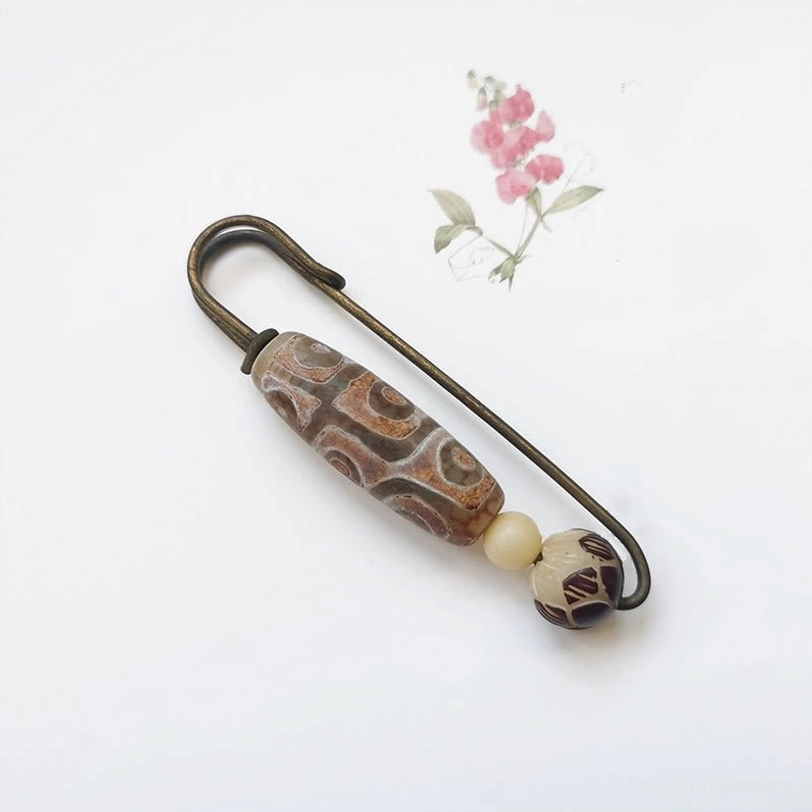 Nine-eye dzi bead bodhi seed brooch side view flat lay on white desktop with bronze safety pin detail