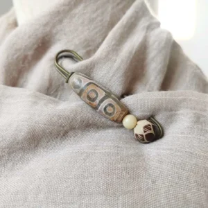 Nine-eye dzi bead brooch styled on neutral linen fabric, demonstrating how to wear tibetan protection brooch on clothing