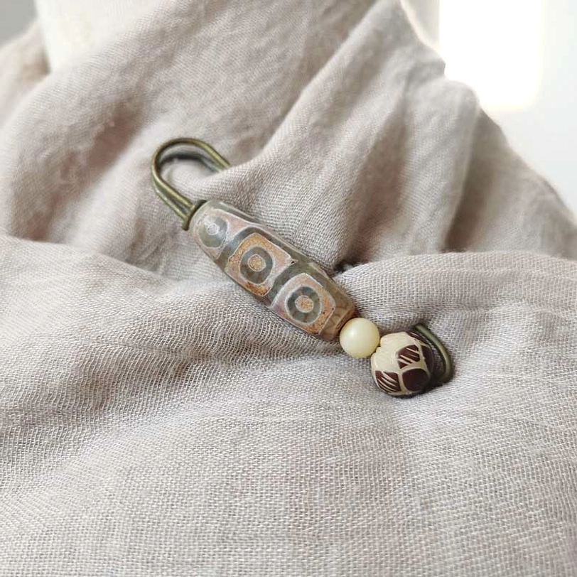 Nine-eye dzi bead brooch styled on neutral linen fabric, demonstrating how to wear tibetan protection brooch on clothing