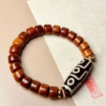 Nine-eye Dzi bone protection bracelet flat lay with red seal stamp on textured paper