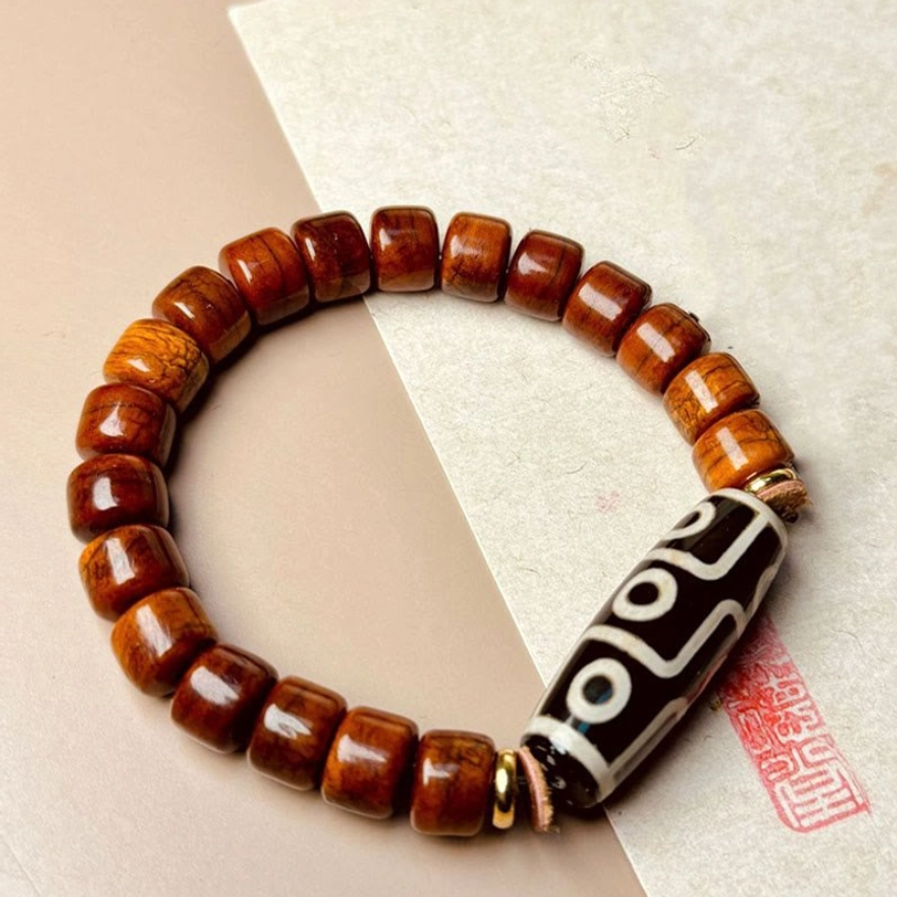 Nine-eye Dzi bone protection bracelet flat lay with red seal stamp on textured paper