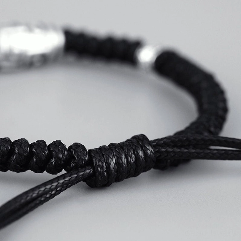 Dzi bracelet adjustable knot detail close-up, showing sliding mechanism with silver accent beads on black braided cord