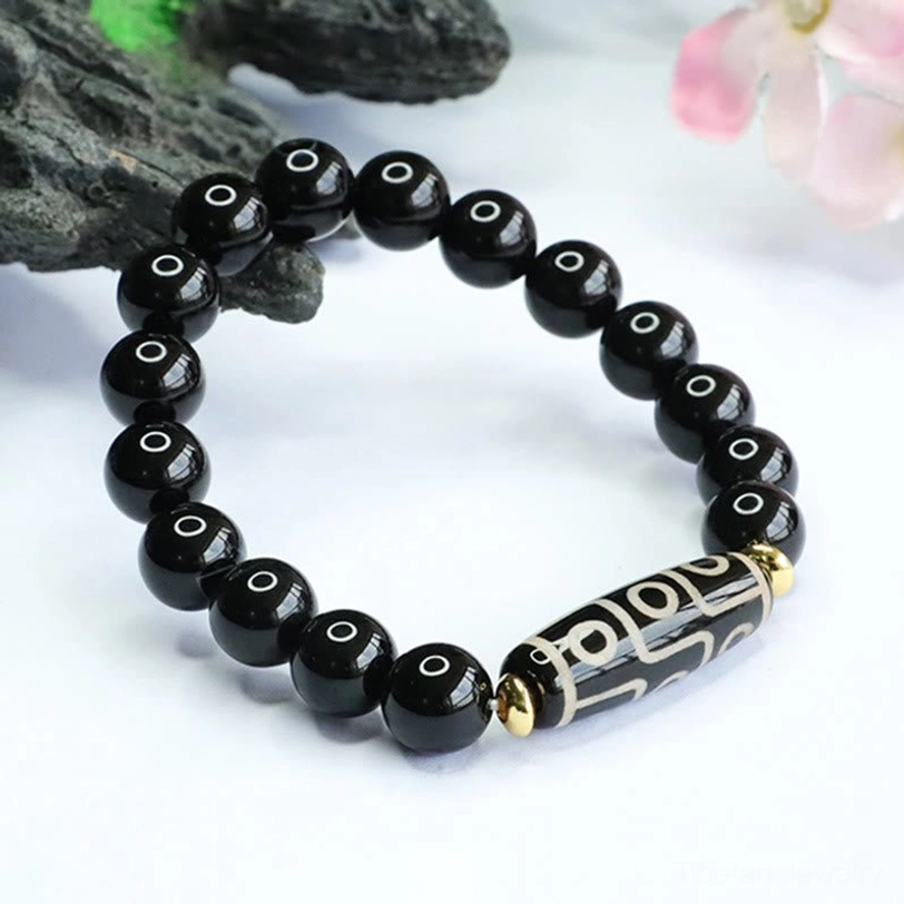 Angled top view of tibetan nine-eye dzi bead bracelet with black onyx stones and gold metal accents on decorative backdrop