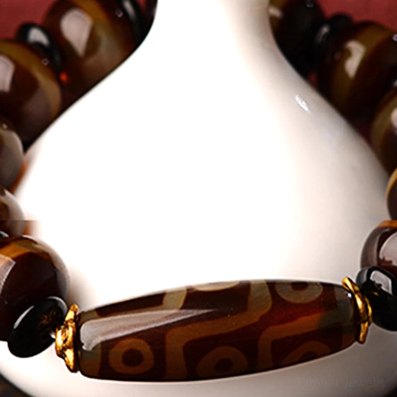 Close-up eye-level view of dzi agate bracelet showcasing detailed nine-eye dzi pattern on agate beads with white ceramic vase background