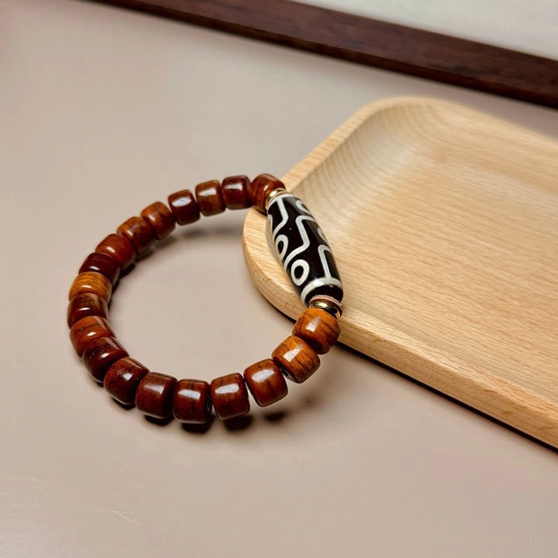 Nine-eye Dzi bead bracelet with dark brown barrel beads on light wooden surface